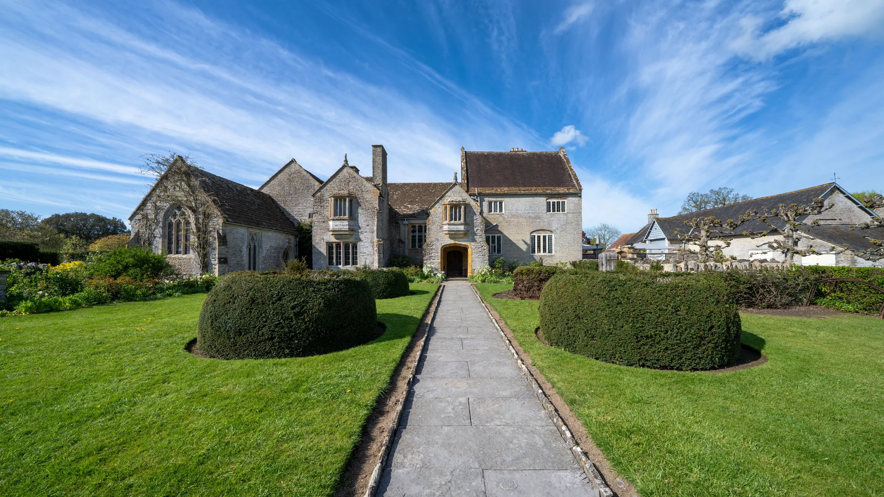 A historic manor house on a mown estate lawn with mature specimen trees